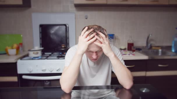 Depressieve man die thuis aan tafel zit, zijn hoofd met zijn handen klemt, camerabeweging - Video