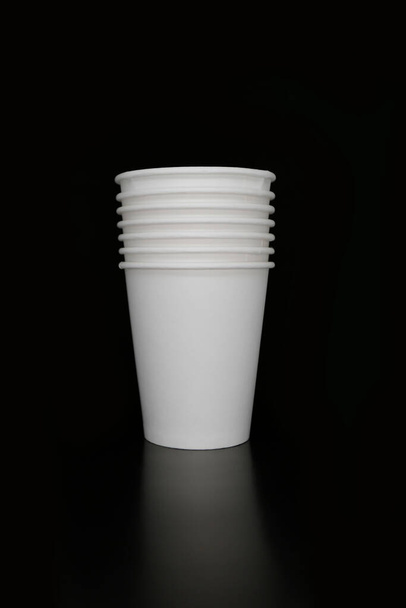 Longa pilha de sete copos de papel branco descartáveis em branco no fundo preto com reflexão, café, chá, beber para ir, levar embora
 - Foto, Imagem