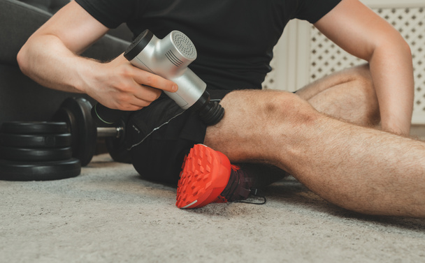 Hombre masaje pierna con dispositivo de percusión de masaje. - Foto, Imagen
