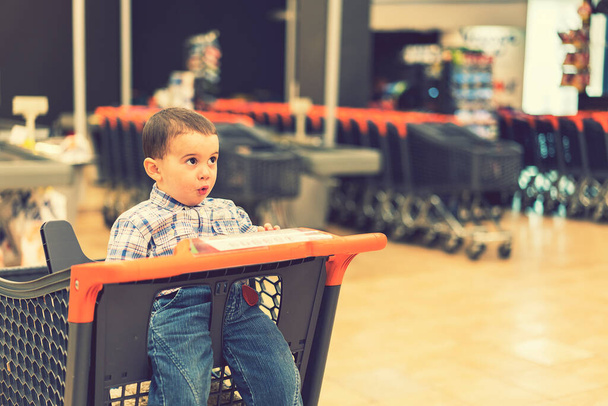 Süpermarketteki el arabasında yeni yürümeye başlayan çocuk. ses tonlu. - Fotoğraf, Görsel