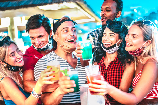 Onnelliset monikansalliset ihmiset juovat yöllä baarissa avoimilla kasvonaamioilla Uusi normaali kesäkonsepti, jossa Millenial ystävät pitävät hauskaa yhdessä Keskity keskimmäiseen kaveriin ja tyttöön, jolla on defocused tausta - Valokuva, kuva