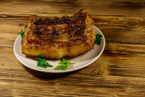 Запечений свинячий живіт в тарілці на дерев'яному столі
 - Фото, зображення