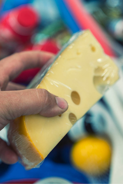 Male hand holds cheese in a supermarket. vertical photo toned. - Photo, Image