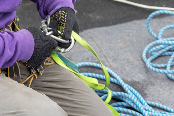 Trabalhador corrige uma corda e equipamento de escalada antes de descer do telhado. Obras de alta altitude
. - Foto, Imagem