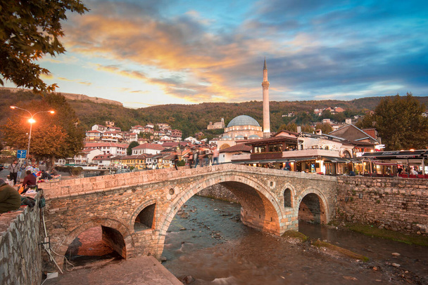 Prizren, Kosowo - 08 lipca 2019: Widok na zachód słońca starego kamiennego mostu i starego osmańskiego meczetu Sinan Pasha. Historyczne miasto położone nad brzegiem rzeki Bistrica - Zdjęcie, obraz