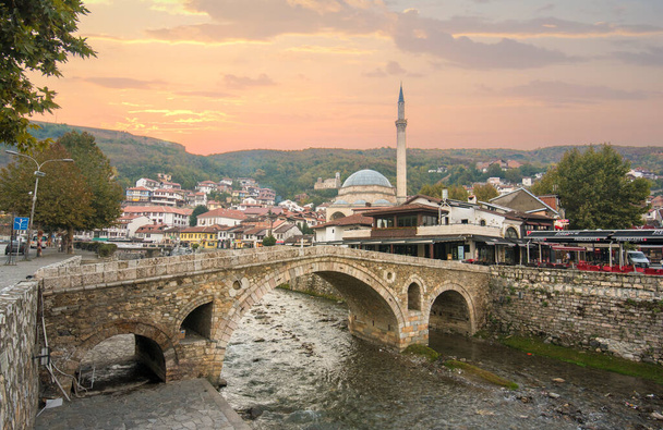 Prizren, Kosovo - 08 July, 2019: Sunset view of old stone bridge and old Ottoman Sinan Pasha Mosque. Historic city located on the banks of the  Bistrica river - Photo, Image