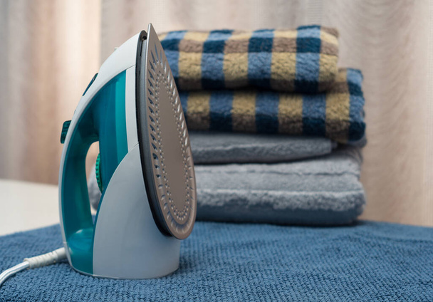 An electric iron stands on a table near clean towels. - Zdjęcie, obraz