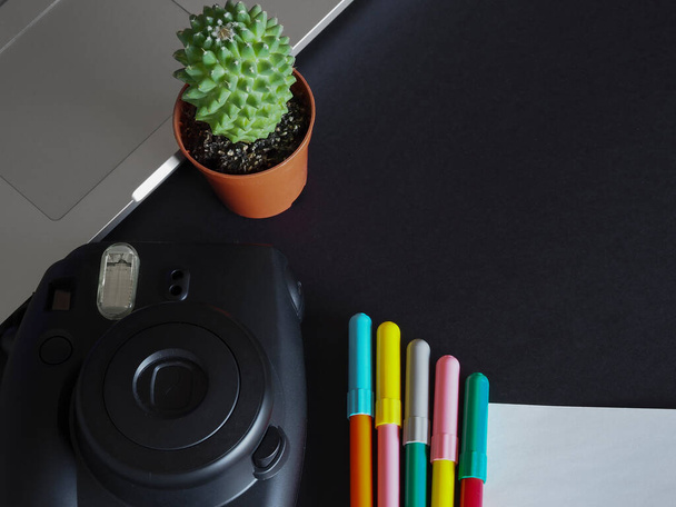 Laptop, hazır kamera, kaktüs, defter, siyah arkaplan üzerine renkli kalem ve kağıt.. - Fotoğraf, Görsel