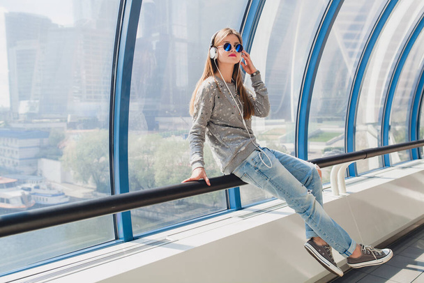 young hipster woman in casual outfit having fun listening to music in headphones, student on vacation, wearing jeans, sweater and sunglasses, urban style - Φωτογραφία, εικόνα