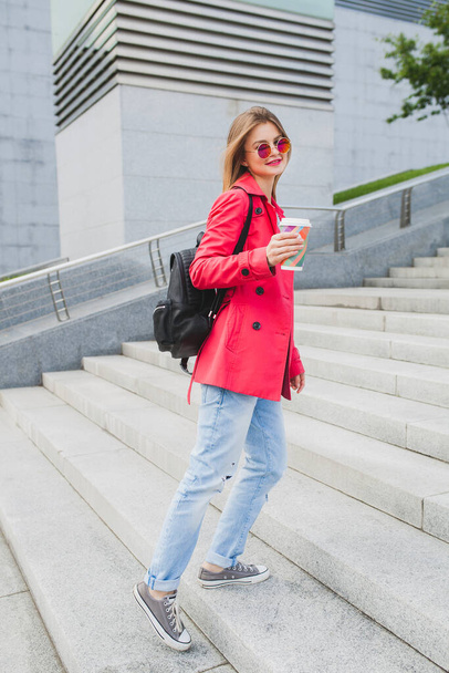 young hipster woman in pink coat, jeans in street with backpack and coffee listening to music on headphones, big city urban style trend, wearing sunglasses - Fotoğraf, Görsel