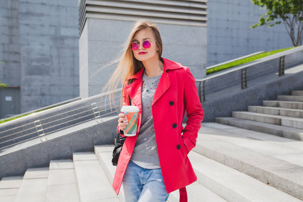 young hipster woman in pink coat, jeans in street with coffee listening to music on headphones, big city urban style trend, wearing sunglasses - Fotoğraf, Görsel