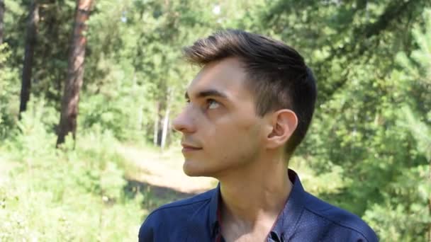 Portrait d'un jeune homme sur fond de feuillage vert - Séquence, vidéo