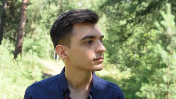 Egy fiatal férfi portréja zöld lombozat hátterében - Felvétel, videó