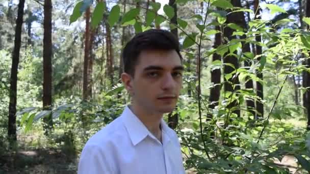 Nuoren miehen muotokuva valkoisessa paidassa metsätaustalla - Materiaali, video