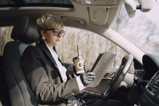 Businesswoman sitting inside a car and drinksa coffee - Foto, Imagen
