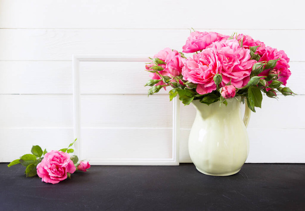 花瓶に写真フレームとピンクのバラの花束。空のブランクモックアップ、背景のホワイトボード、ポスター製品デザイン - 写真・画像