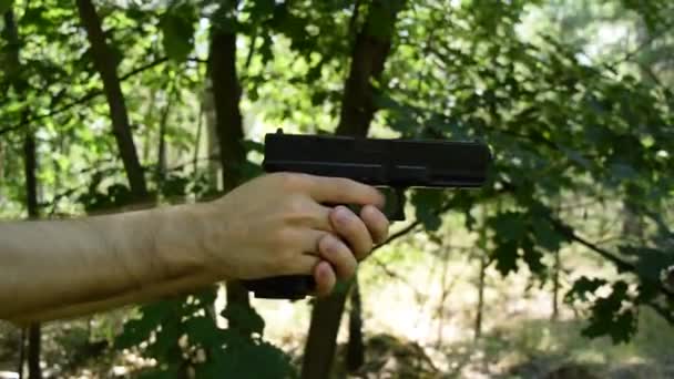 Vista de las manos con un arma sobre un fondo de follaje verde en el bosque
 - Metraje, vídeo