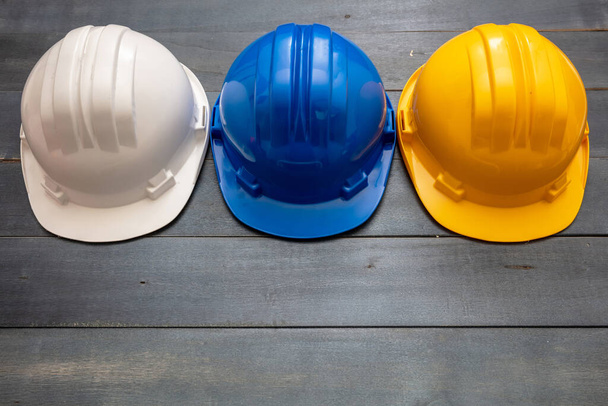 Work safety protection equipment. Industrial protective hardhats white, yellow and blue colors on wooden background. Personal health and safety concept. - Photo, Image