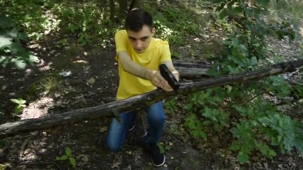 Ο νεαρός με το κίτρινο μπλουζάκι πυροβολεί με ένα πιστόλι στο δάσος. - Πλάνα, βίντεο