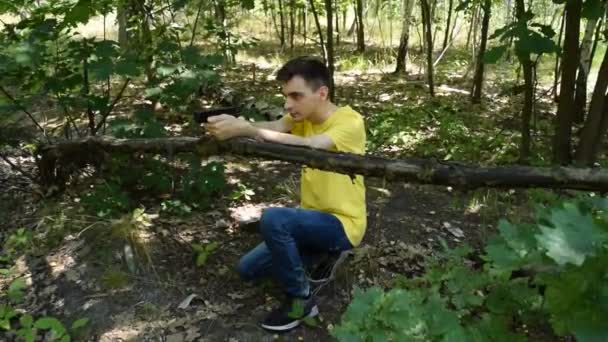 Ο νεαρός με το κίτρινο μπλουζάκι πυροβολεί με ένα πιστόλι στο δάσος. - Πλάνα, βίντεο