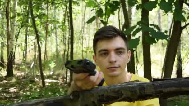 Młody mężczyzna w żółtej koszulce strzela z pistoletu w lesie - Materiał filmowy, wideo