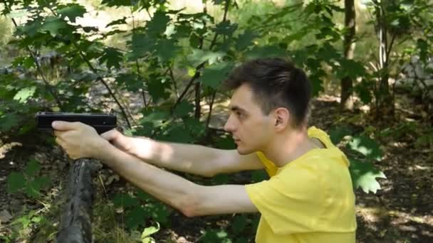 黄色のTシャツの若者が森の中でピストルで撃つ - 映像、動画