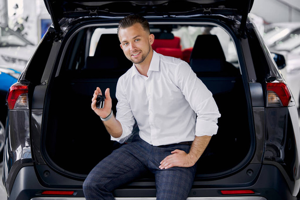 portrait of smiling businessman on the trunk of automobile in dealership - Photo, Image