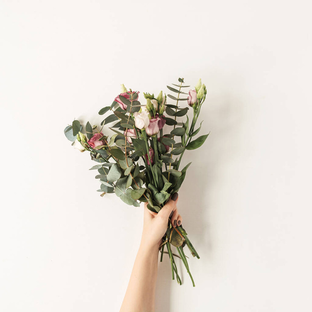 Vrouwelijke hand met kleurrijke rozen bloemen boeket tegen witte muur. Feestelijke feestdagen feestelijk bloemconcept - Foto, afbeelding