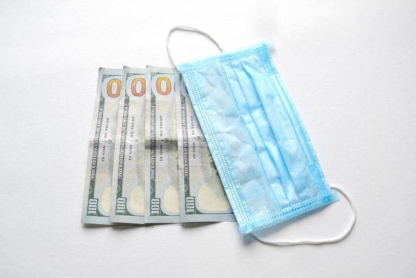 Chirurgische gezichtsmaskers en Amerikaanse dollars bankbiljetten, opgeblazen in- en uitvoer, verplichte maskering, covid-19 en coronavirus - Foto, afbeelding