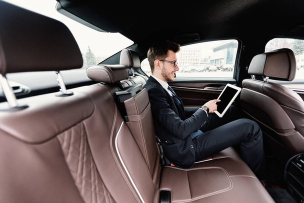 Νεαρός επιχειρηματίας που χρησιμοποιεί το ψηφιακό tablet του σε πολυτελές αυτοκίνητο - Φωτογραφία, εικόνα