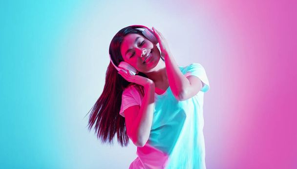 Užijte si tanec. Šťastná asijská dívka se drží za ruce na sluchátka a poslouchá hudbu - Fotografie, Obrázek