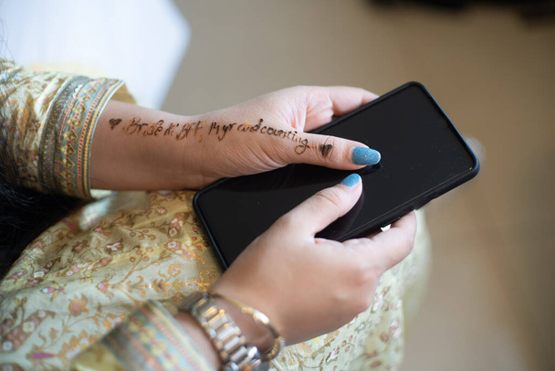 Menina indiana jovem decorado em vestido de ouro branco se preparando para um casamento segurando telefone com palavras noiva para ser BFF escrito em tatuagem henna
 - Foto, Imagem