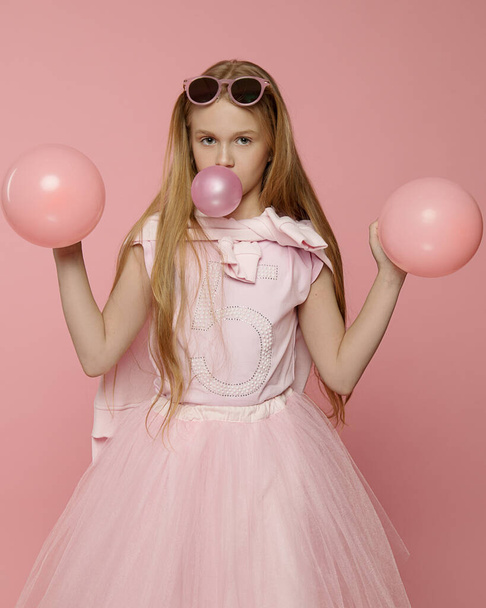 Beautiful funny girl 10 years old sunglasses and pink balloons in hands make bubble gum in Studio on the background. Concept close-up photo advertising gum, organization of holidays. Positive emotions - Foto, Imagem