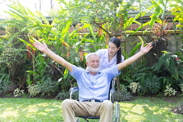 Eine Krankenschwester pflegt einen Senioren im Rollstuhl in seinem Garten zu Hause - Foto, Bild