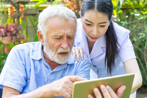 Krankenschwester hilft Rentner bei der Arbeit mit Laptop im Hinterhof - Foto, Bild
