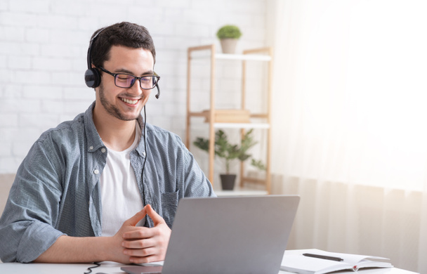 Apprendre l'anglais en ligne. Un gars souriant avec des écouteurs regardant un ordinateur portable, parlant avec un professeur - Photo, image