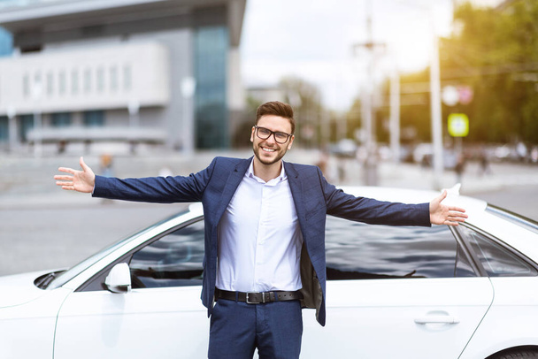Uśmiechnięty lider firmy stojący z otwartymi ramionami przed samochodem na ulicy miejskiej - Zdjęcie, obraz