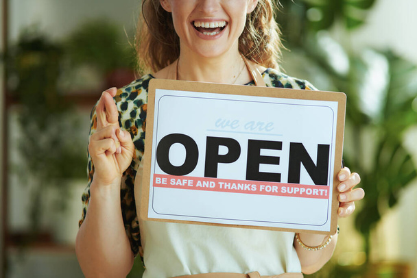Opening small business after covid-19 pandemic. Closeup on smiling middle aged small business owner woman in apron with crossed fingers showing open sign. - Foto, immagini