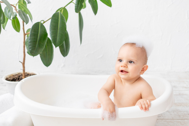 A small child boy 8 months old bathes in a bath with foam and soap bubbles, place for text - Φωτογραφία, εικόνα