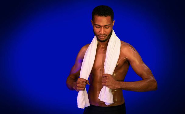 Muskulöser Kerl mit Handtuch posiert im Studio vor blauem Hintergrund - Foto, Bild