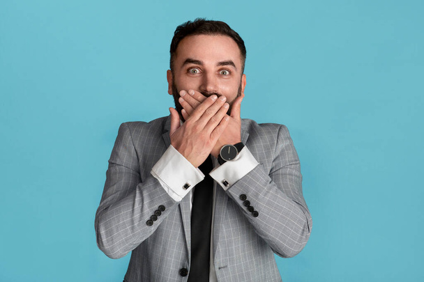 Millenniumi üzletember fedi száját meglepetés kék háttér - Fotó, kép