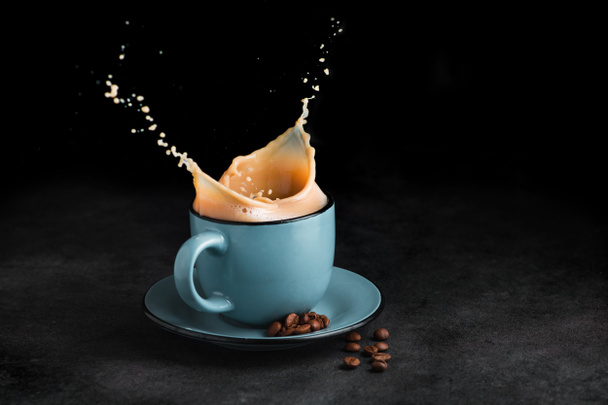 Koude koffie splash in een blauwe beker op stenen tafel, zwarte achtergrond. Begrip "verse drank" - Foto, afbeelding