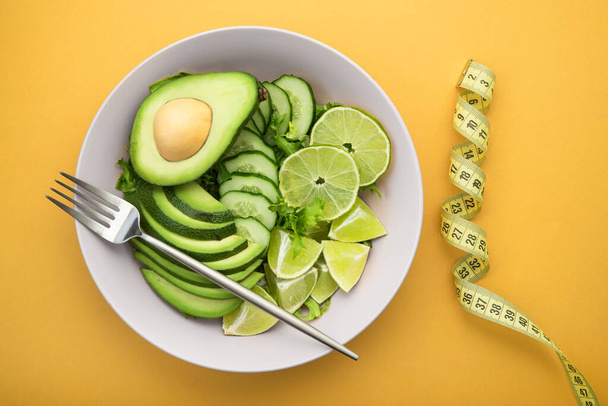 Fresh salad with avocado, green lime and cucumber on a pastel yellow background. Diet concept food. top view - Photo, Image