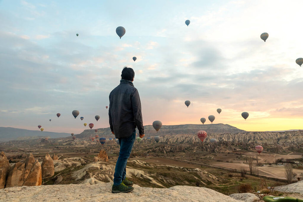 24 Şubat 2018: Kapadokya Vadisi üzerinde uçan harika balonlarla vadi manzarasının tadını çıkaran adam. Goreme, Kapadokya, Türkiye - Fotoğraf, Görsel