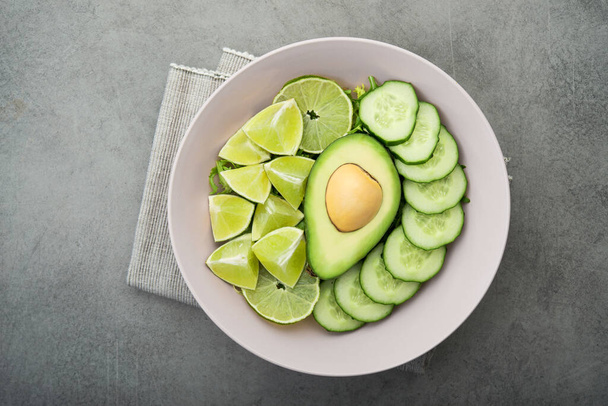 Φρέσκια σαλάτα με αβοκάντο, πράσινο λάιμ και αγγούρι σε γκρι πέτρινο τραπέζι. Vegan φόντο τροφίμων. πάνω όψη - Φωτογραφία, εικόνα