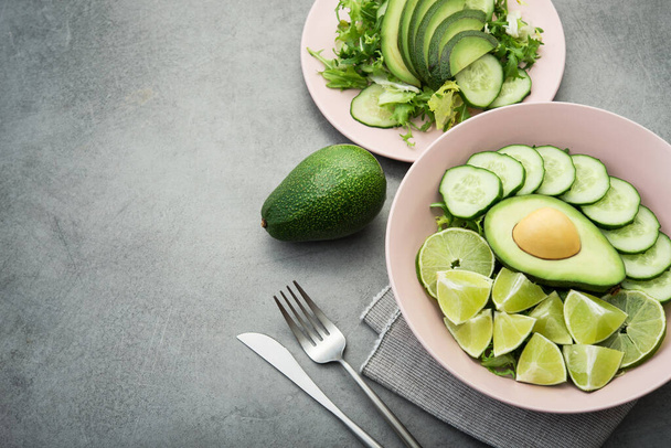 Fresh salad with avocado, green lime and cucumber on a gray stone table. Vegan food background - Foto, Imagem