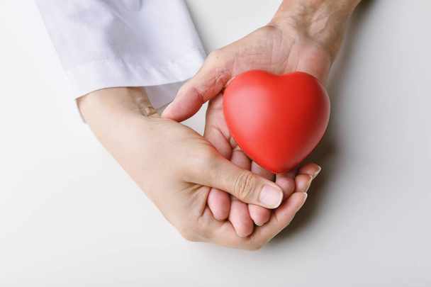 Liebe und Gesundheitskonzepte, Rotes Herz in den Händen, Arzt hält älteren Patienten die Hand zur Unterstützung, Organspende und Wohltätigkeit im Gesundheitswesen. - Foto, Bild