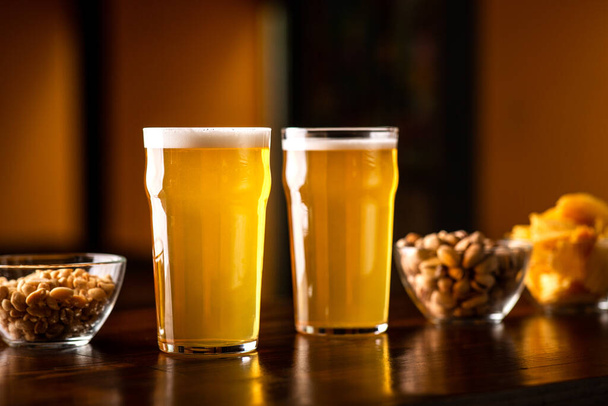 El negocio de la cerveza en el bar. Vasos de cerveza, pistachos, papas fritas y nueces en mesa de madera en el interior
 - Foto, imagen