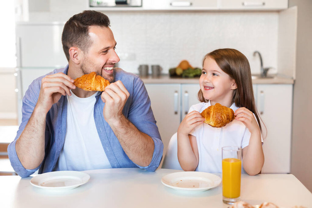 Otec a dcera mají croissanty k snídani sedí v kuchyni - Fotografie, Obrázek