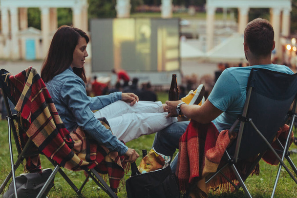 Şehir parkında kamp sandalyelerinde oturan çift açık hava sinemasında film seyrediyor. - Fotoğraf, Görsel